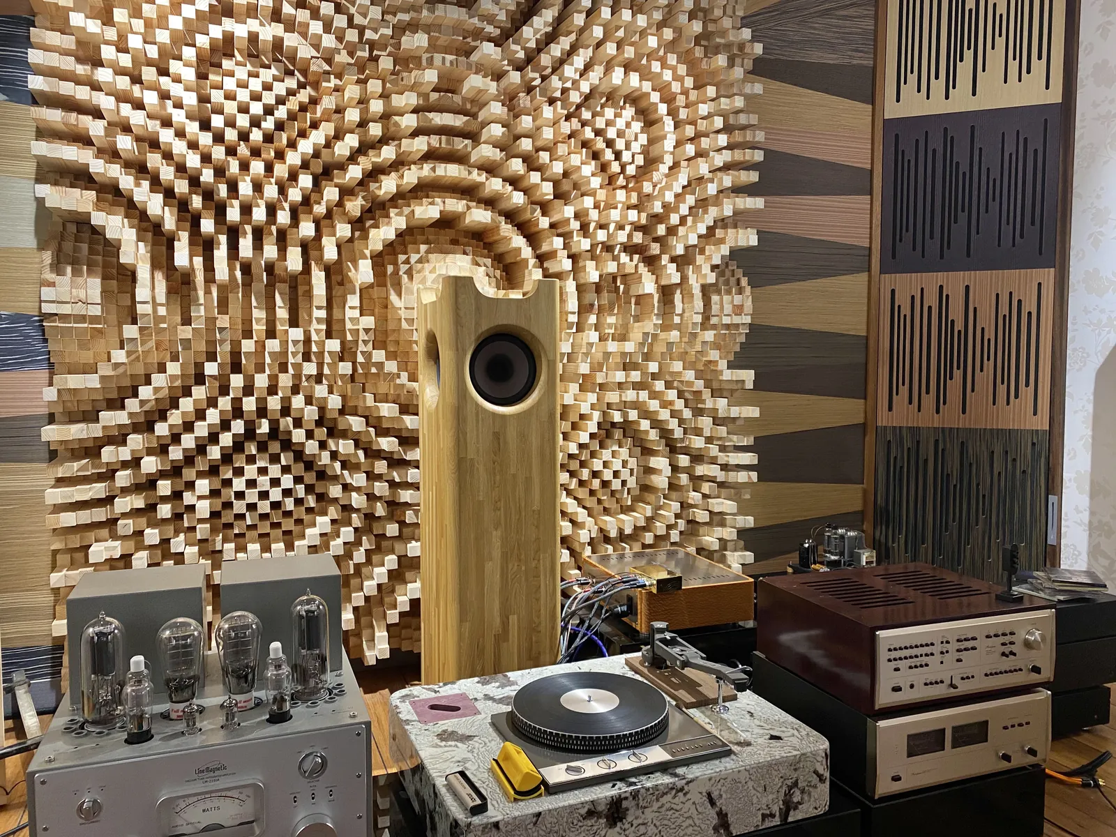 Single Speaker Stereo loudspeaker positioned in front of an acoustic diffuser wall among audio equipment